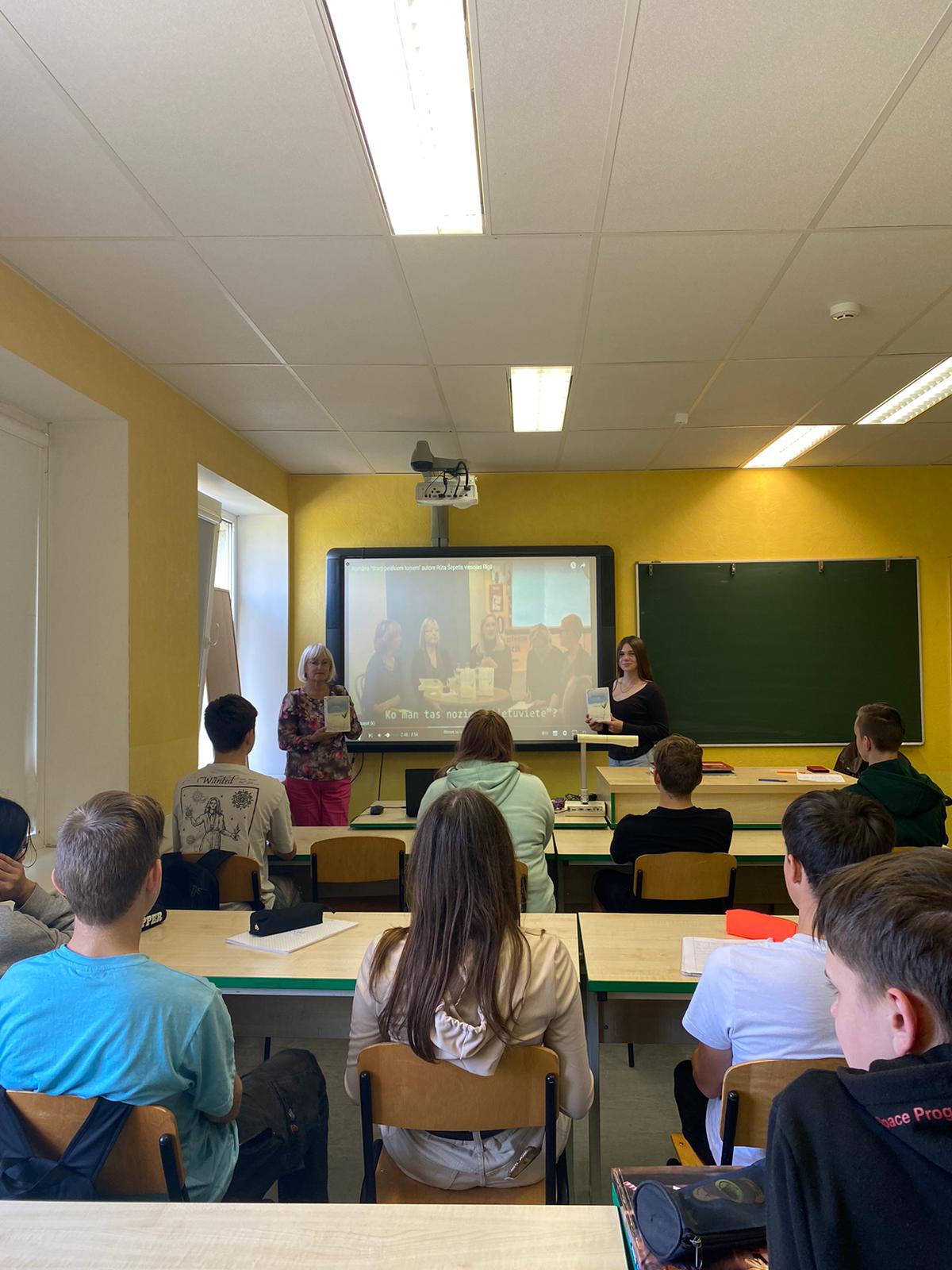 Skolotāja ar grāmatu stāv pie projektora