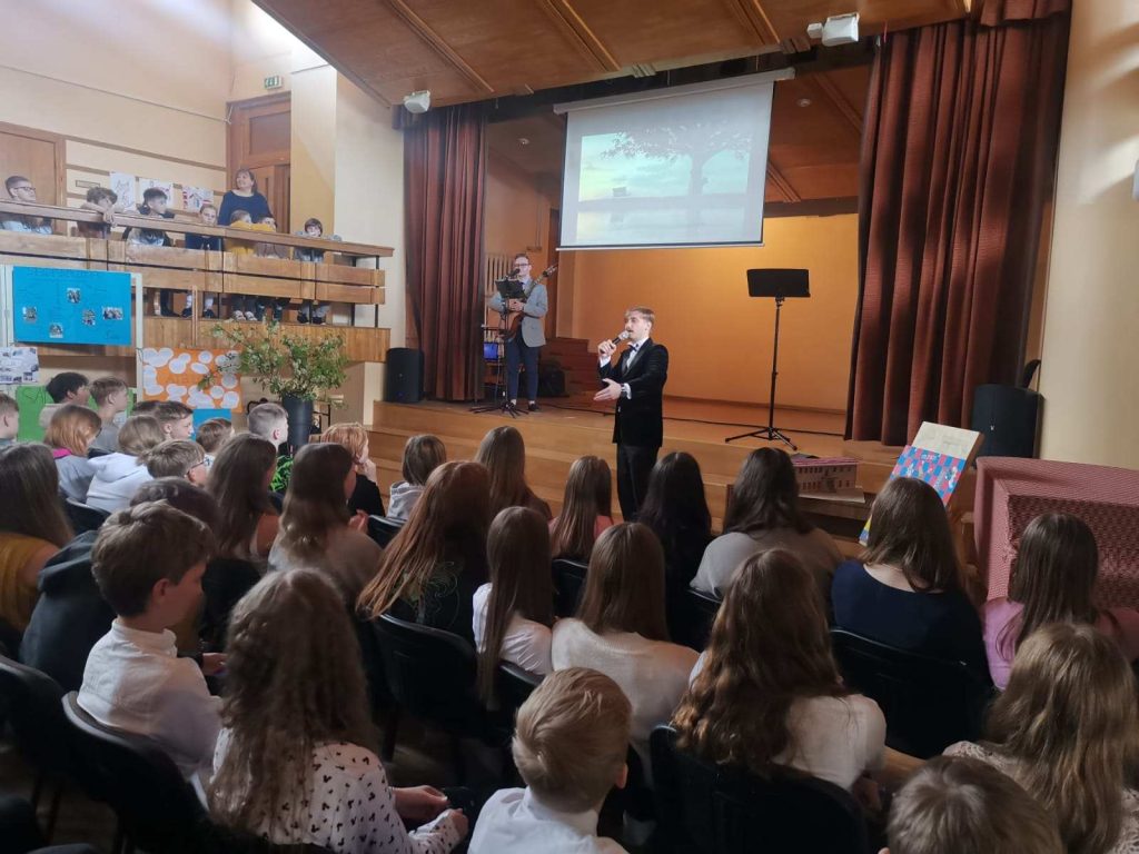Koncerts, vīrietis dzied mikrofonā, vīrietis spēlē''gitāru,skatuve skatītāji