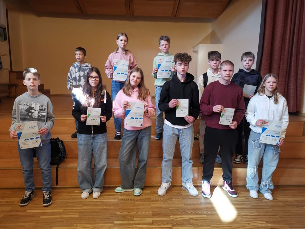 Bērni stāv uz skatuves kāpnēm, rokās diplomi