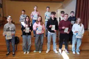 Bērni stāv uz skatuves kāpnēm, rokās diplomi