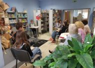Bibliotēka, istabas augs, grāmatau plaukti, skolēni ar grāmatām, žūrija, skaļā lasīšana