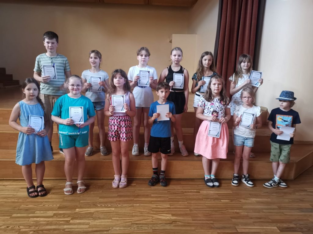 Bērni ar diplomiem rokās stāv uz skatuves podestiem