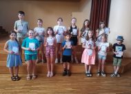Bērni ar diplomiem rokās stāv uz skatuves podestiem
