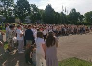 Skolēni stāv pusaplī, pie skolas, mācību gada noslēgums, skolēni svinīgi tērpti
