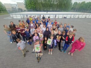 Bērni pozē sporta laukumā, priecīgi rāda diplomus